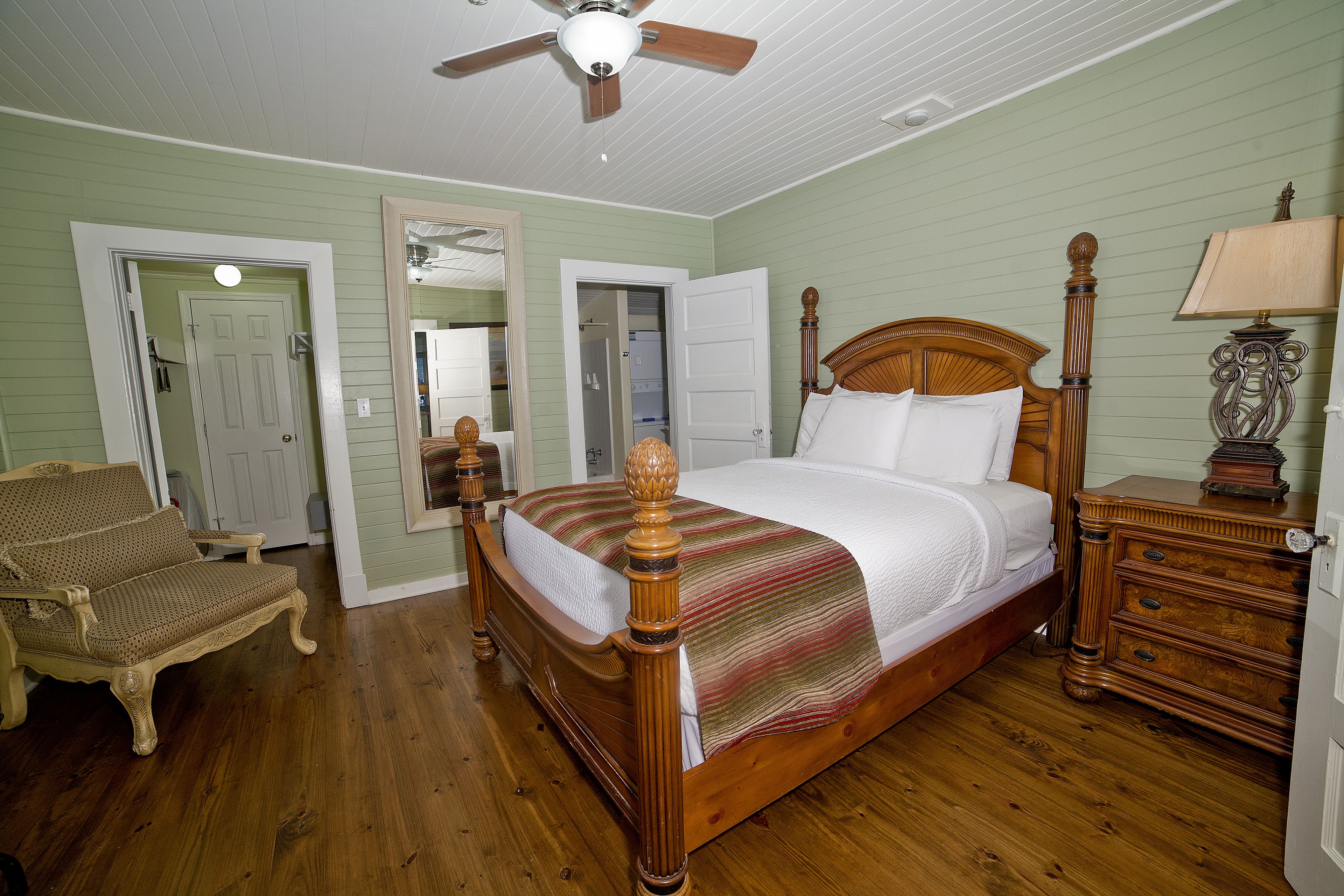 A bedroom with a wooden bed, a wooden nightstand, a chair, and a ceiling fan.