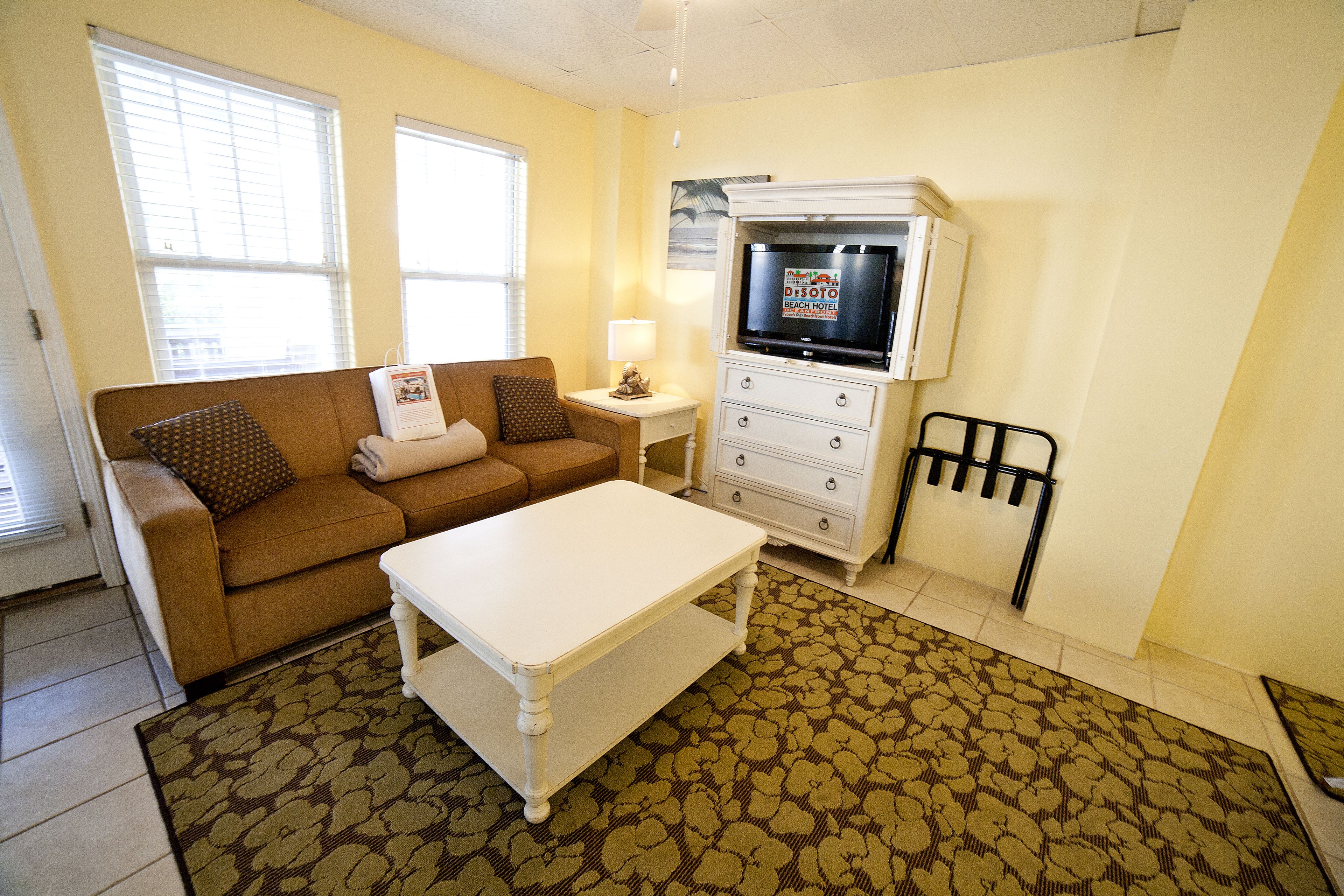 A living room with a brown sofa, a white coffee table, a TV on a stand, and a patterned rug.