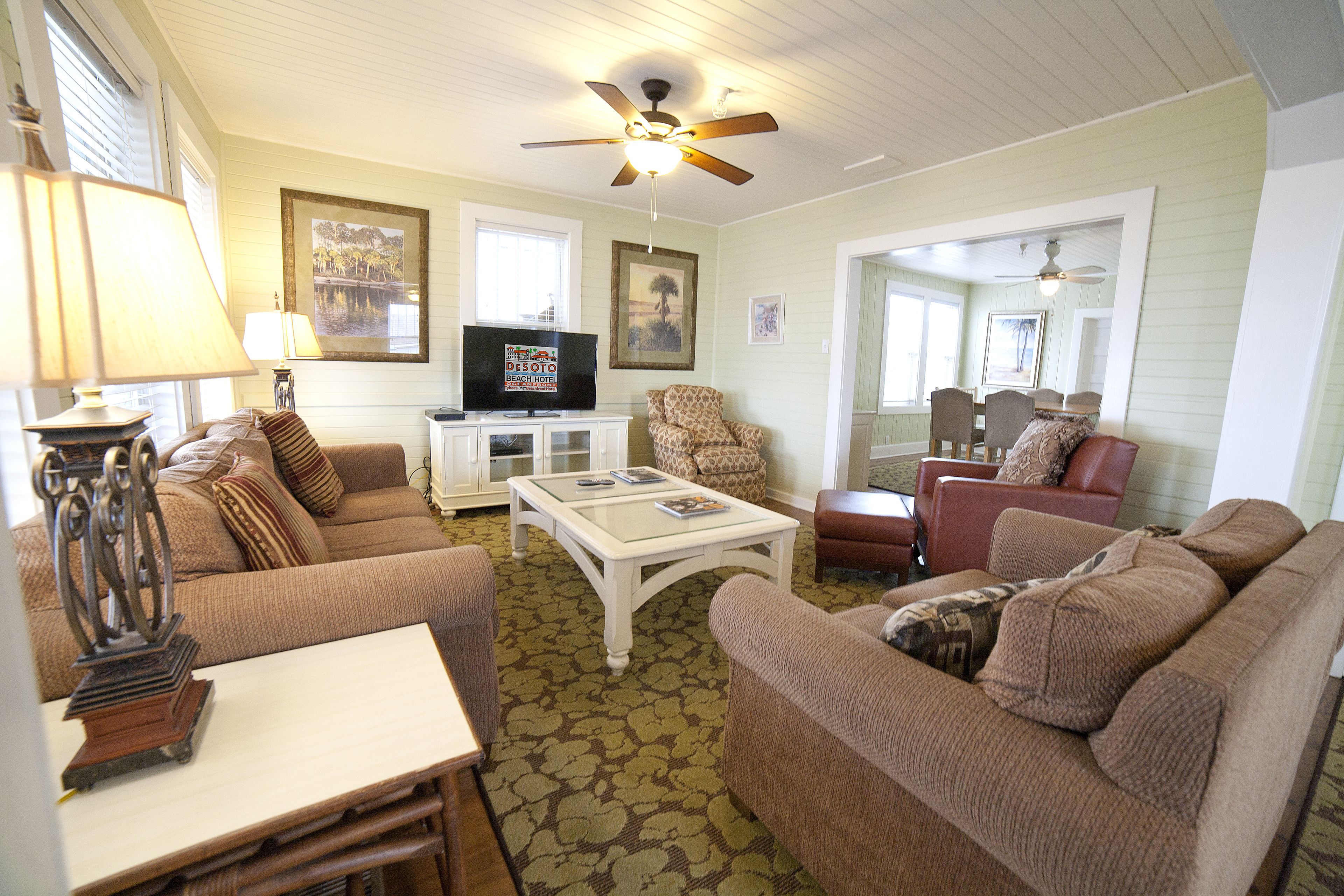 A living room with a ceiling fan, a television, and a dining area with a table and chairs.
