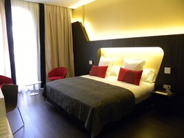 A modern hotel room with a large bed, red and white pillows, a red chair, and a desk.