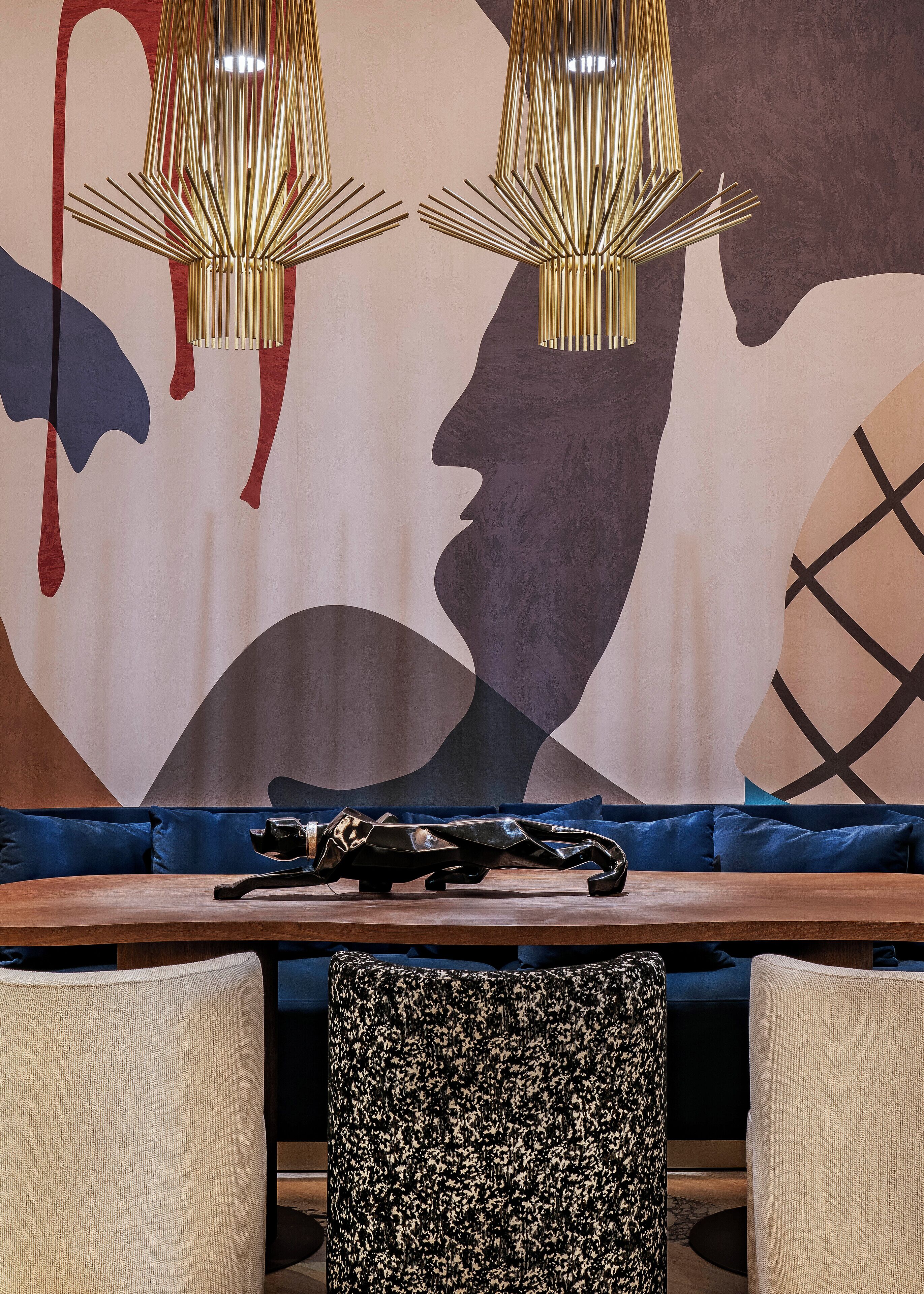 Un intérieur moderne agrémenté d’œuvres d’art abstraites sur les murs, d’une table en bois et de sièges recouverts d’un tissu bleu.