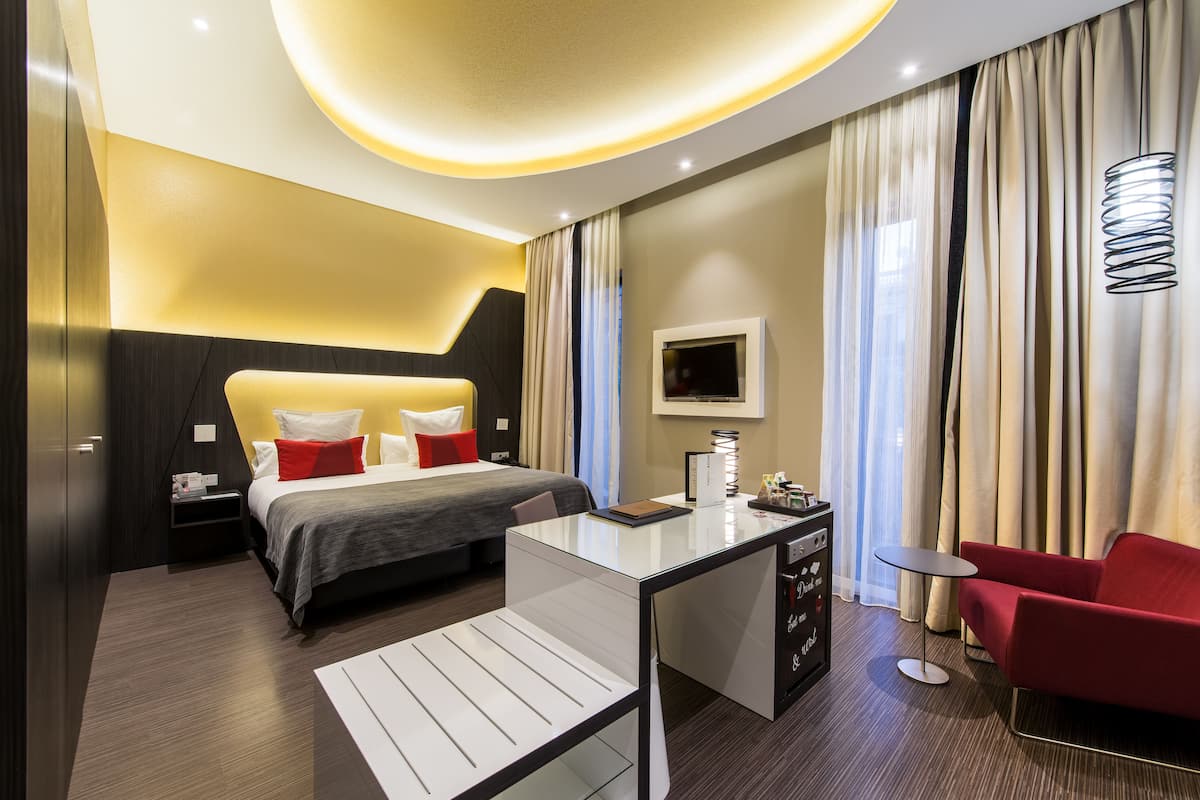 A modern hotel room with a bed, desk, chair, and a TV.