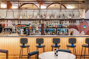 Uma área de bar com balcão de madeira, vários bancos e uma variedade de garrafas e copos.