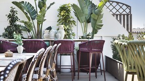 A rooftop terrace with wicker chairs, a dining table, and large potted plants. - Hotel Vincci Gala (Barcelona)