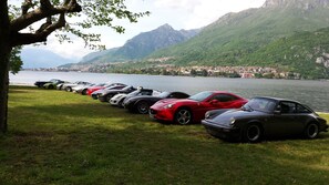 A row of luxury sports cars parked on a grassy area by a lake with mountains in the background. - Hotel Resort Nautilus (Mandello del Lario)