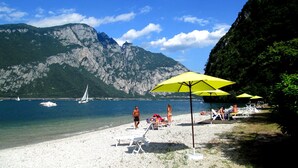 A beach with white sand, a yellow umbrella, and a mountain in the background. - Hotel Resort Nautilus (Mandello del Lario)
