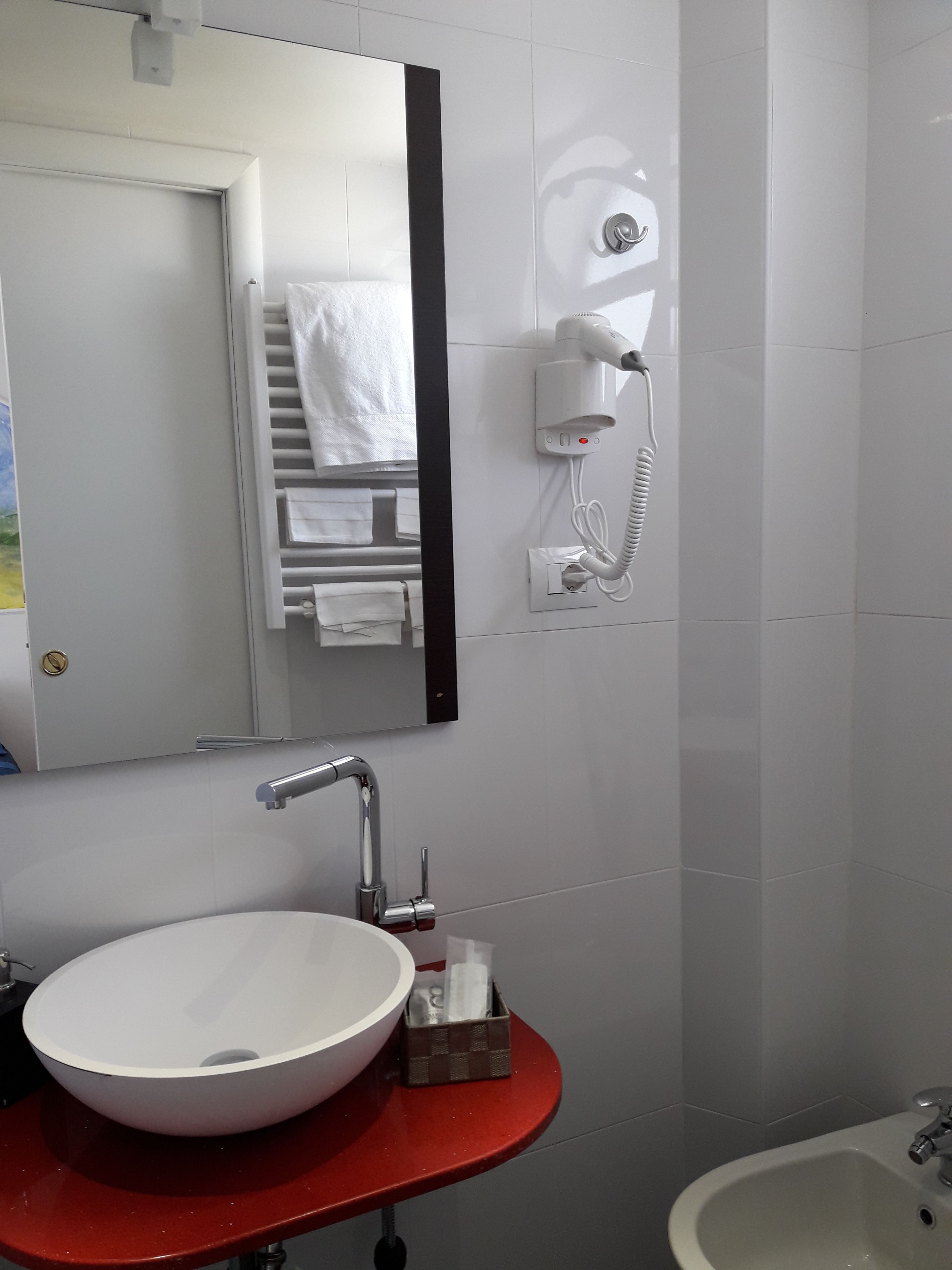 A bathroom with a white sink, a red countertop, a mirror, a towel rack, and a handheld hair dryer mounted on the wall.