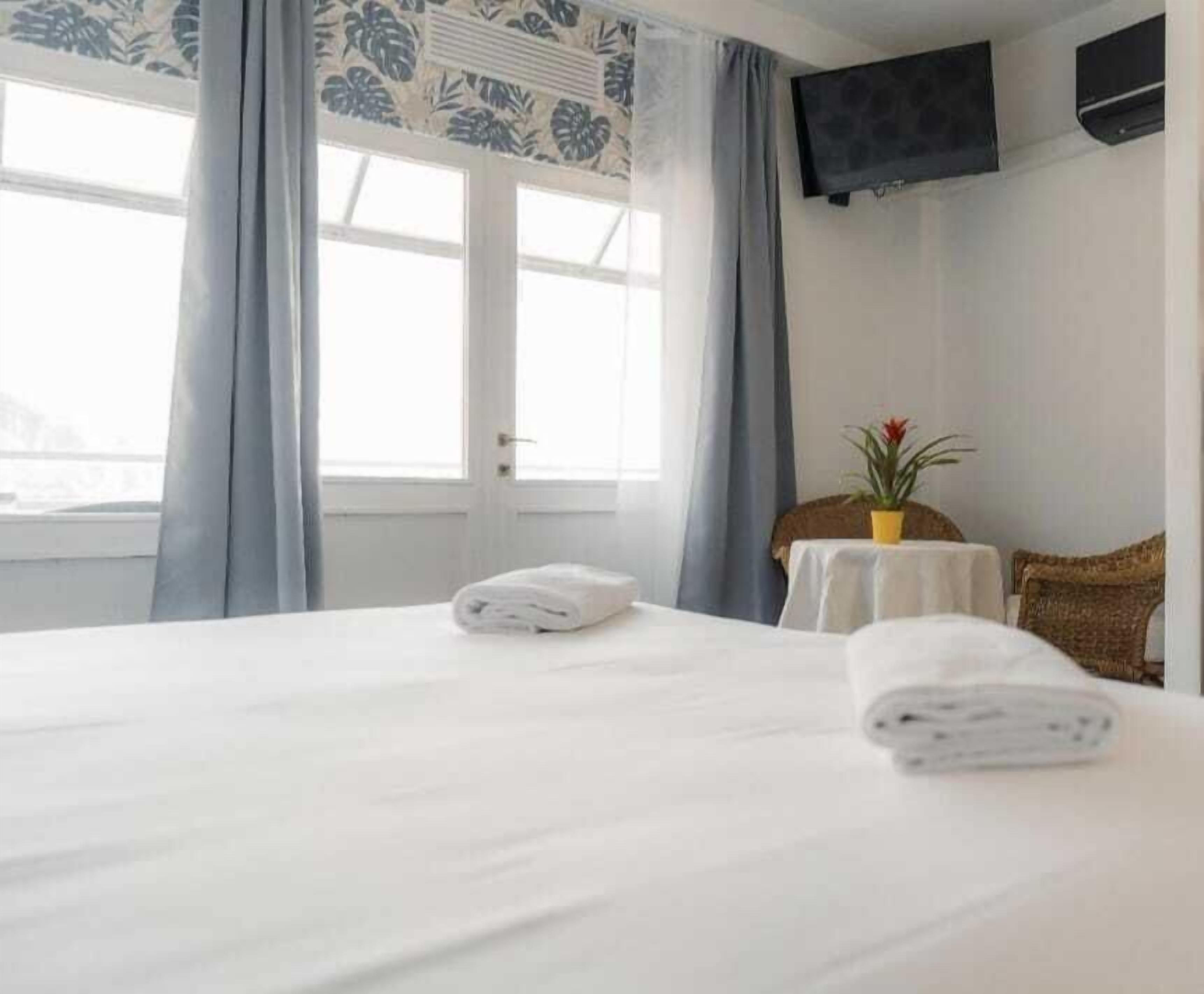 Ein Hotelzimmer mit Bett, kleinem Tisch mit Pflanze, Fernseher an der Wand und Fenster mit Vorhängen.