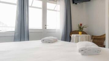 Ein Hotelzimmer mit Bett, kleinem Tisch mit Pflanze, Fernseher an der Wand und Fenster mit Vorhängen.