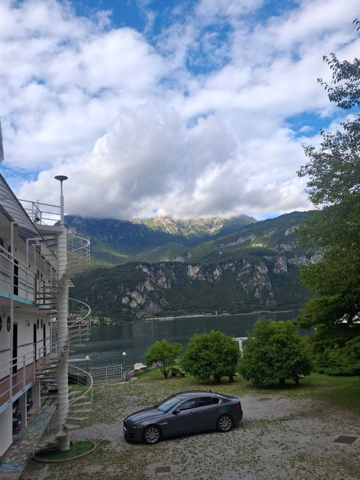 Un edificio con escalera de caracol, un coche estacionado al frente y vistas a montañas y un lago.