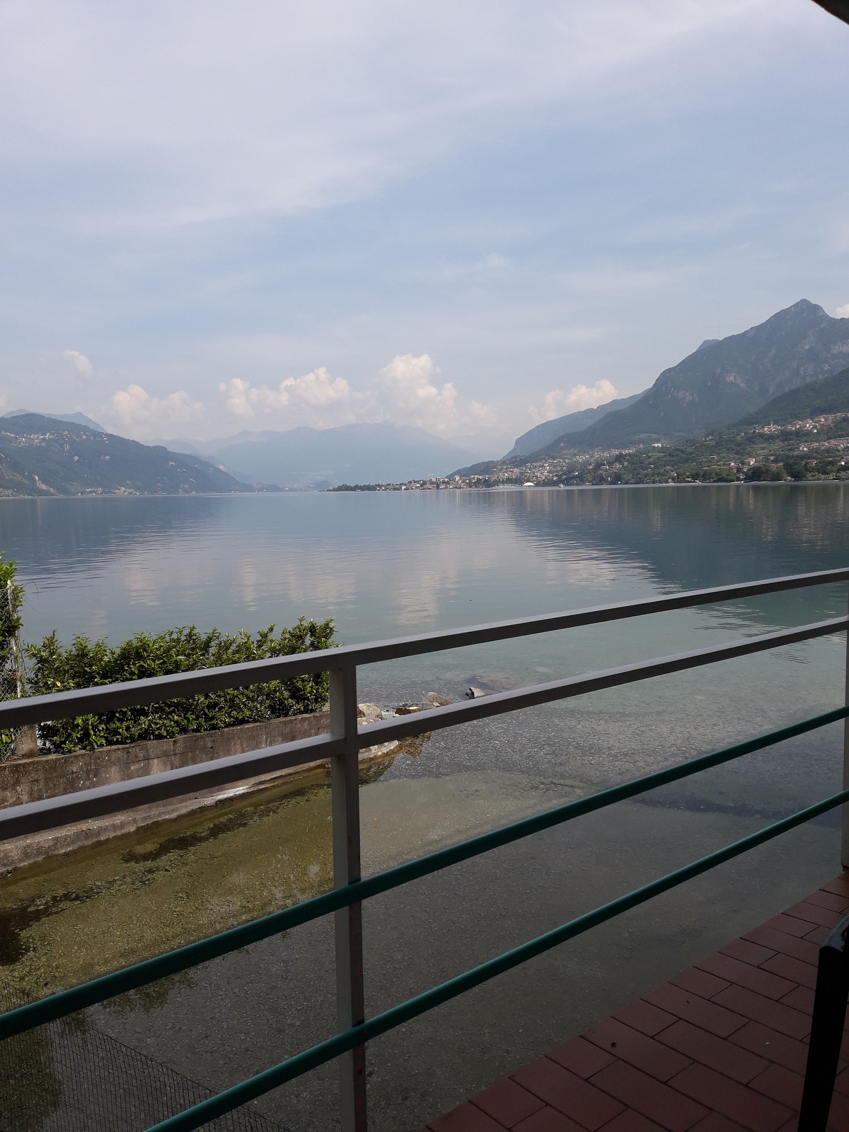 A view of a lake with mountains in the background, a clear sky, and a railing in the foreground.