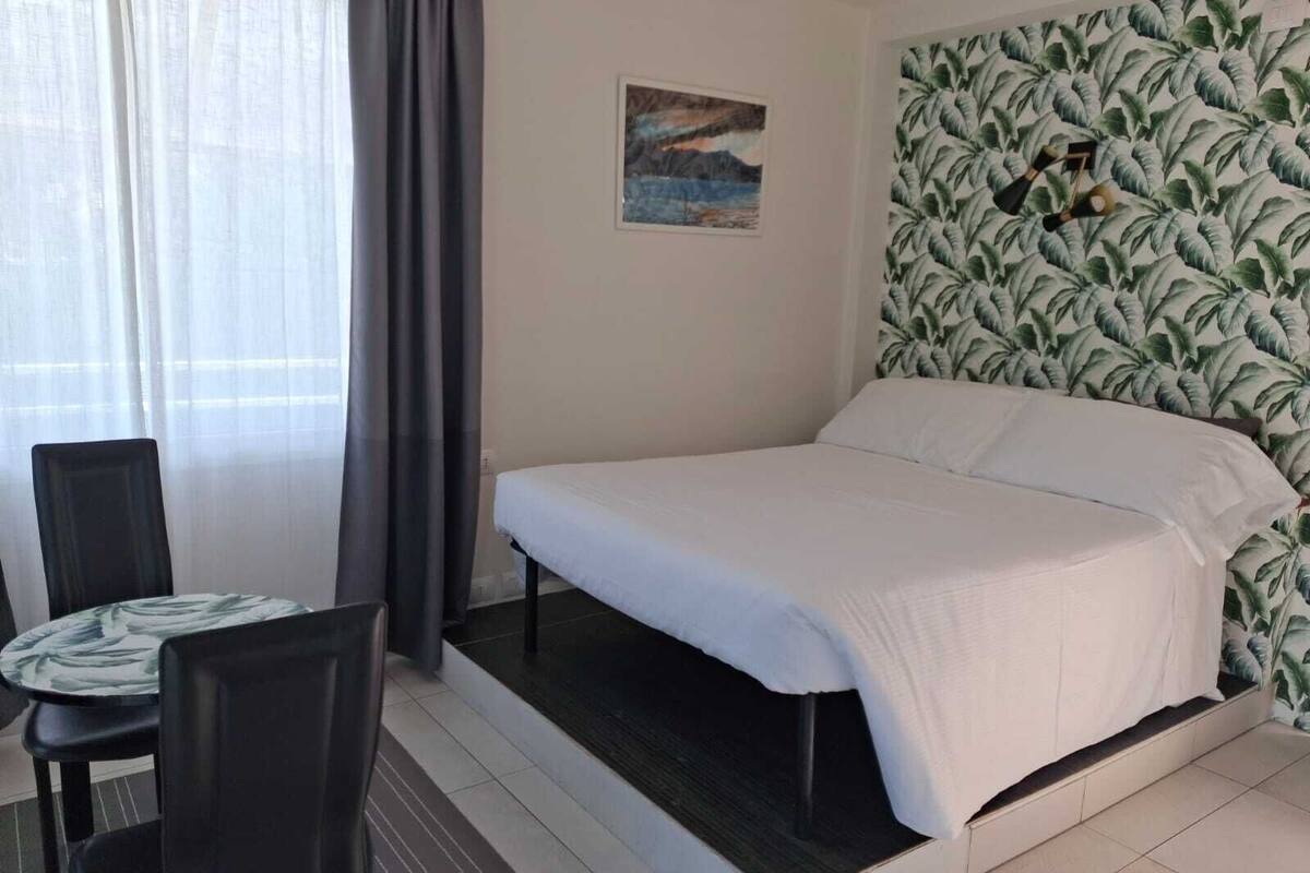 Un dormitorio con cama, una silla, una mesa y un papel tapiz tropical.