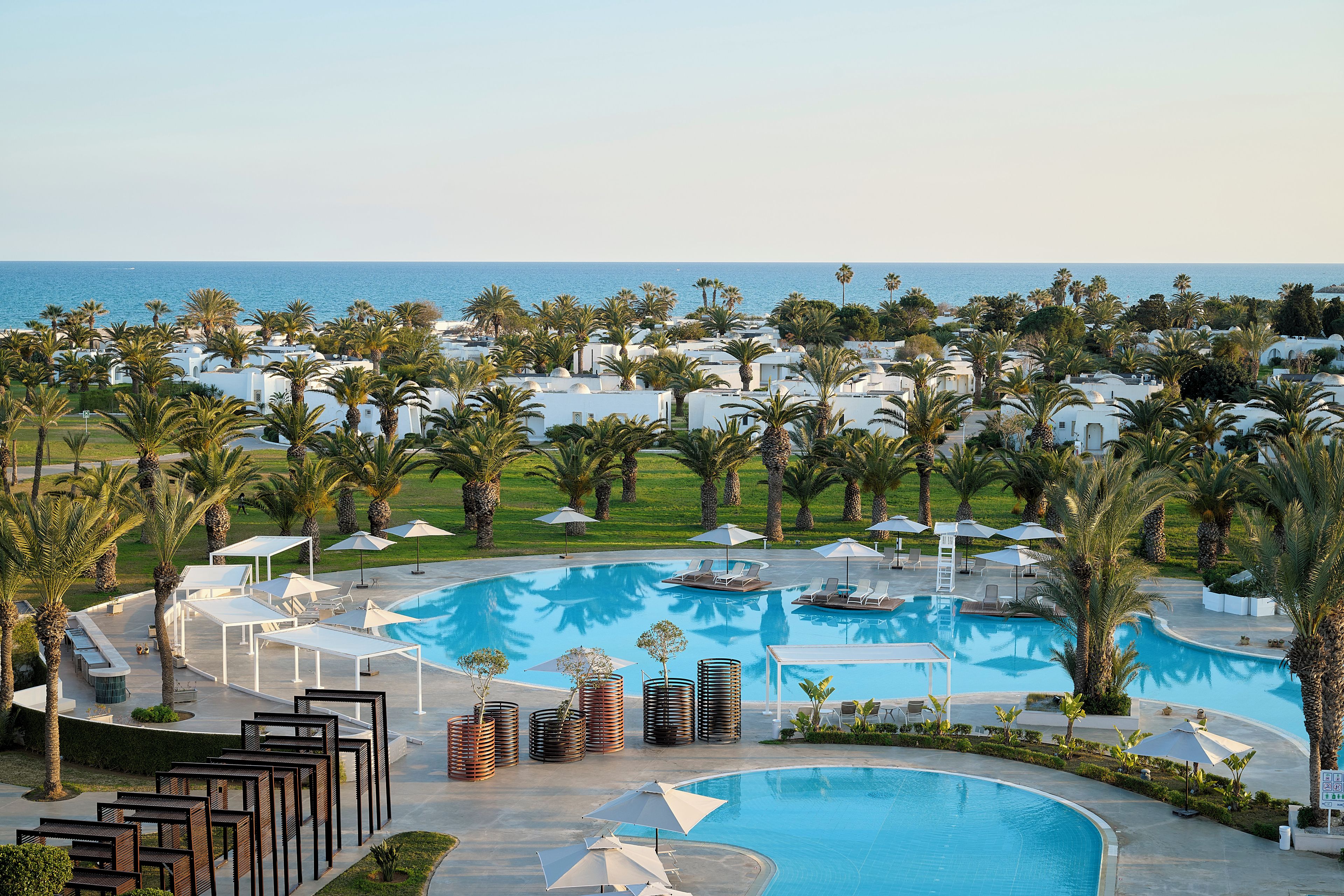 Een resort met een groot zwembad, palmbomen en uitzicht op zee.