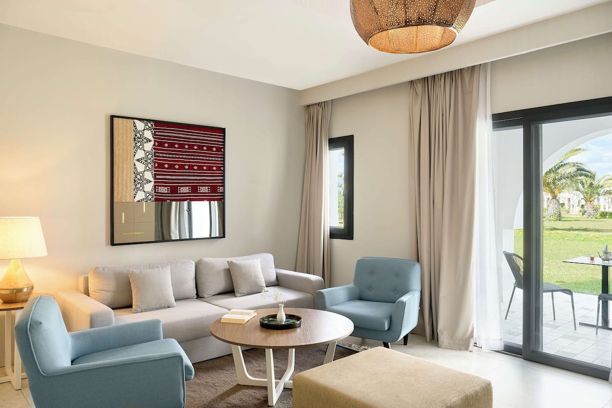 A modern living room with a sofa, two armchairs, a coffee table, and a large window with a view of the outdoors.