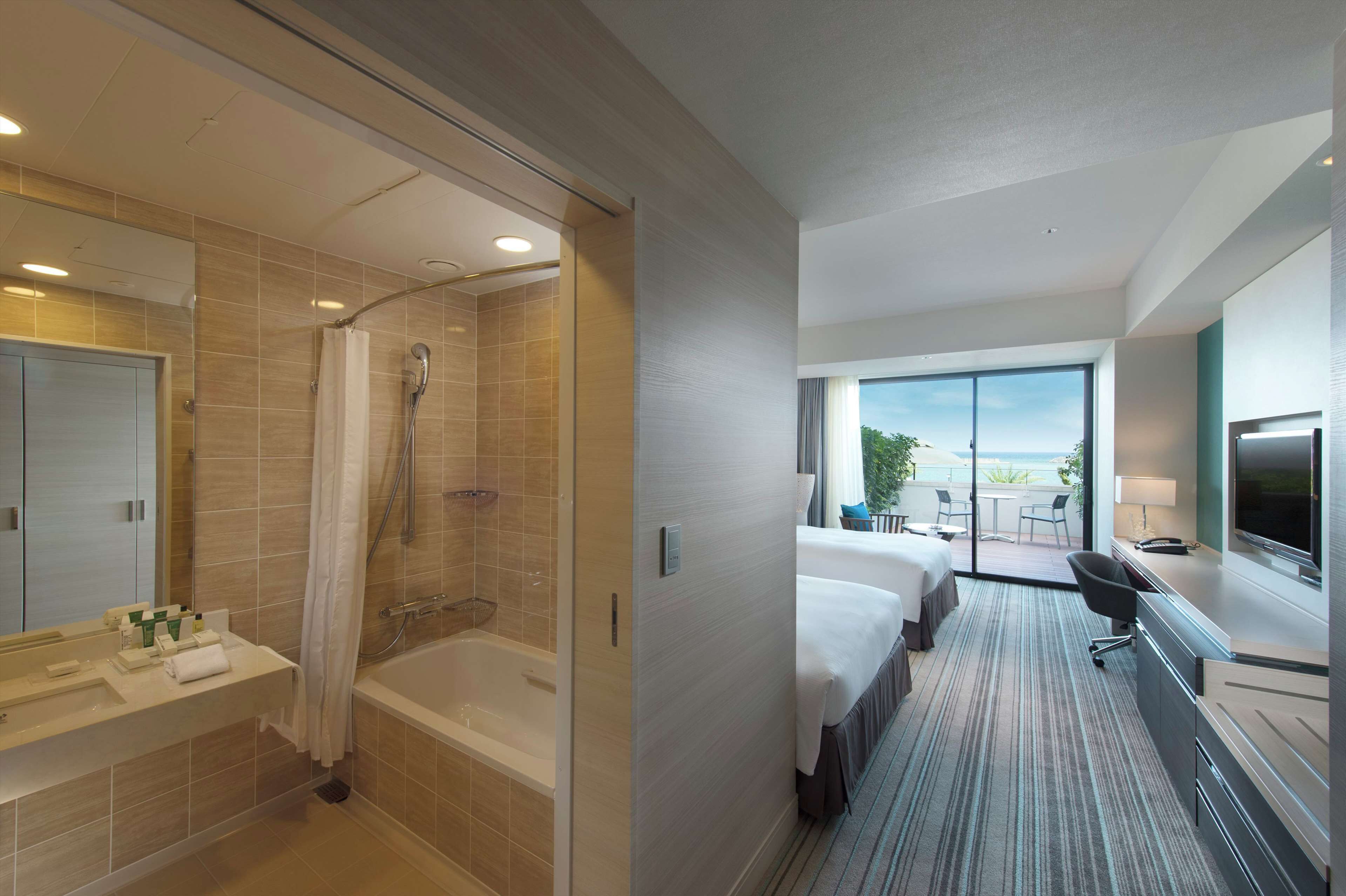 A modern hotel room with a shower, bathtub, two beds, a desk, and a large window with a view.