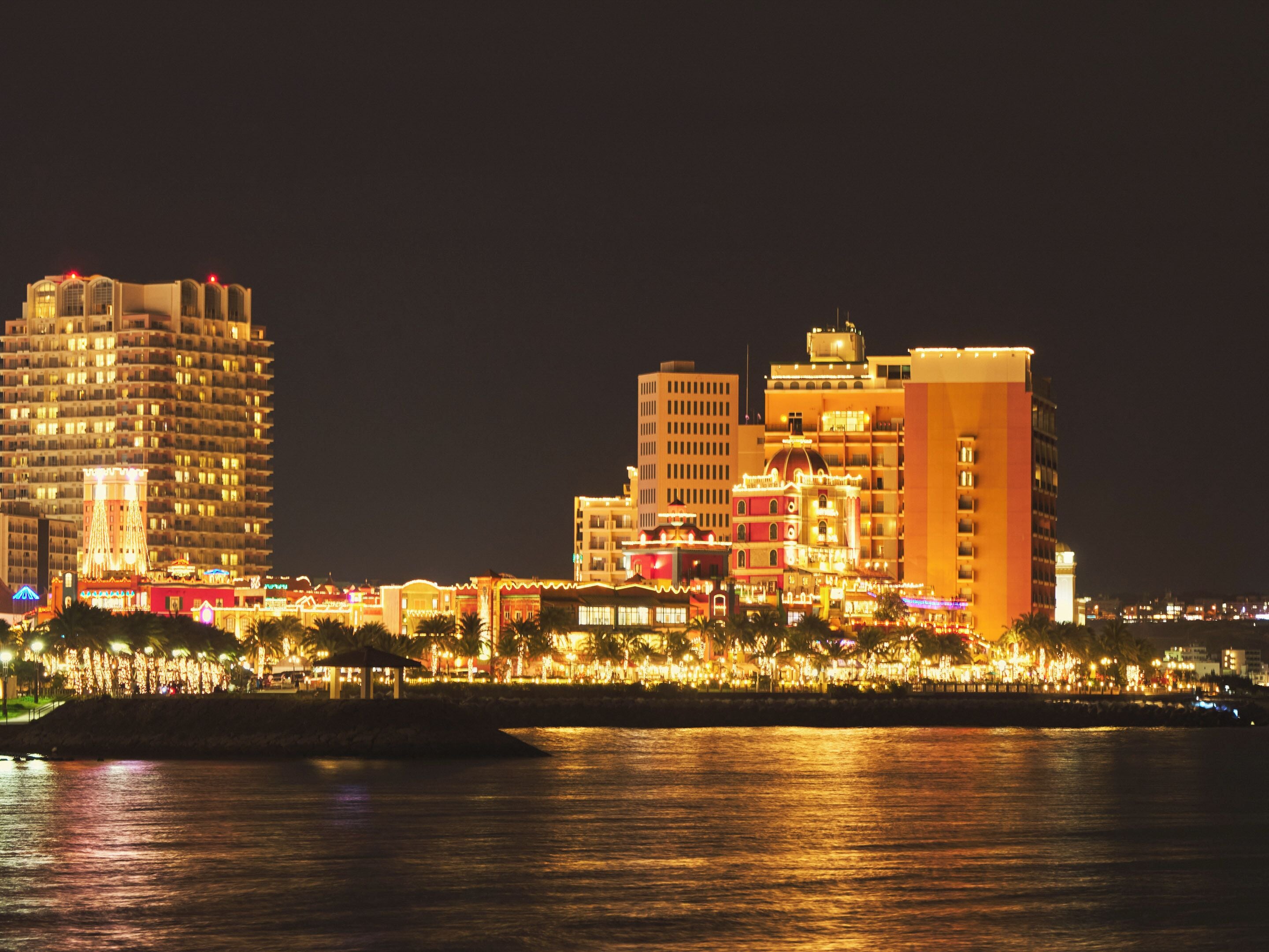 A waterfront hotel with multiple high-rise buildings, a marina, and a well-lit promenade.