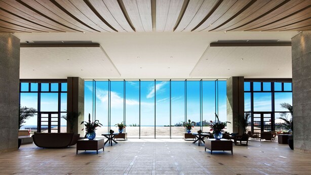 Um hall amplo com vista para a praia, mobiliário moderno e teto de madeira.