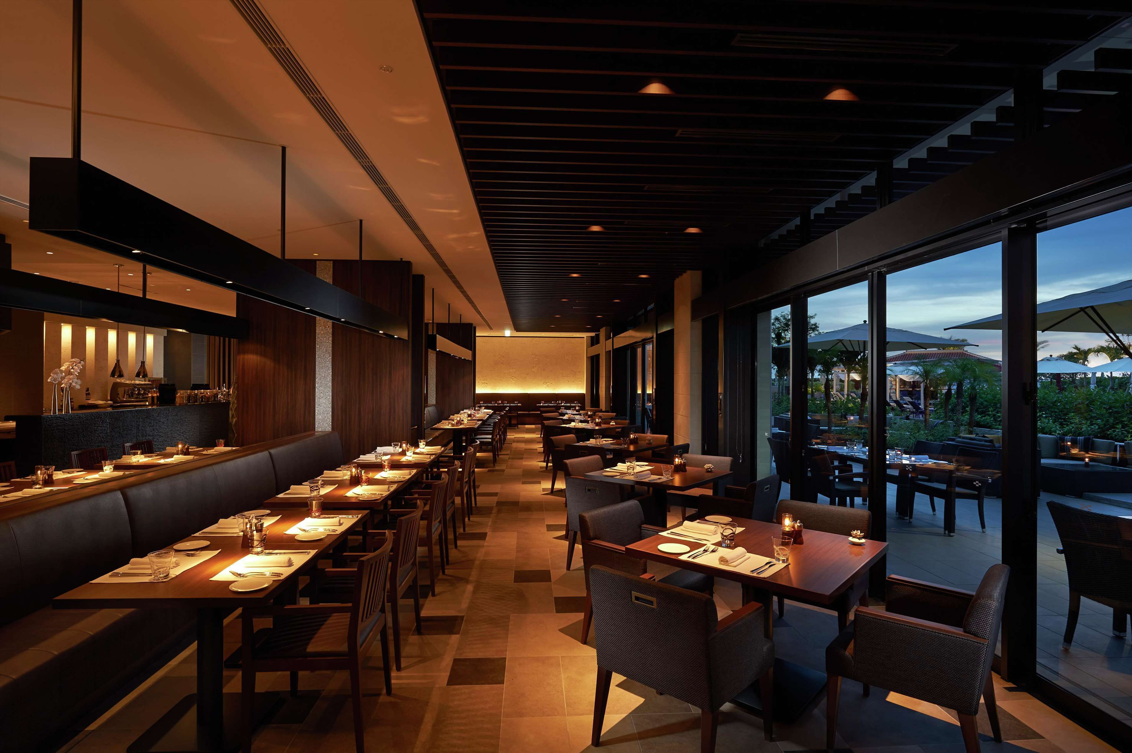 A modern restaurant with a long counter and booths, large windows, and a view of the outdoors.