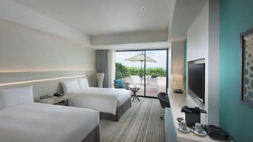 A hotel room with two beds, a desk, a TV, and a balcony with a table and chairs.