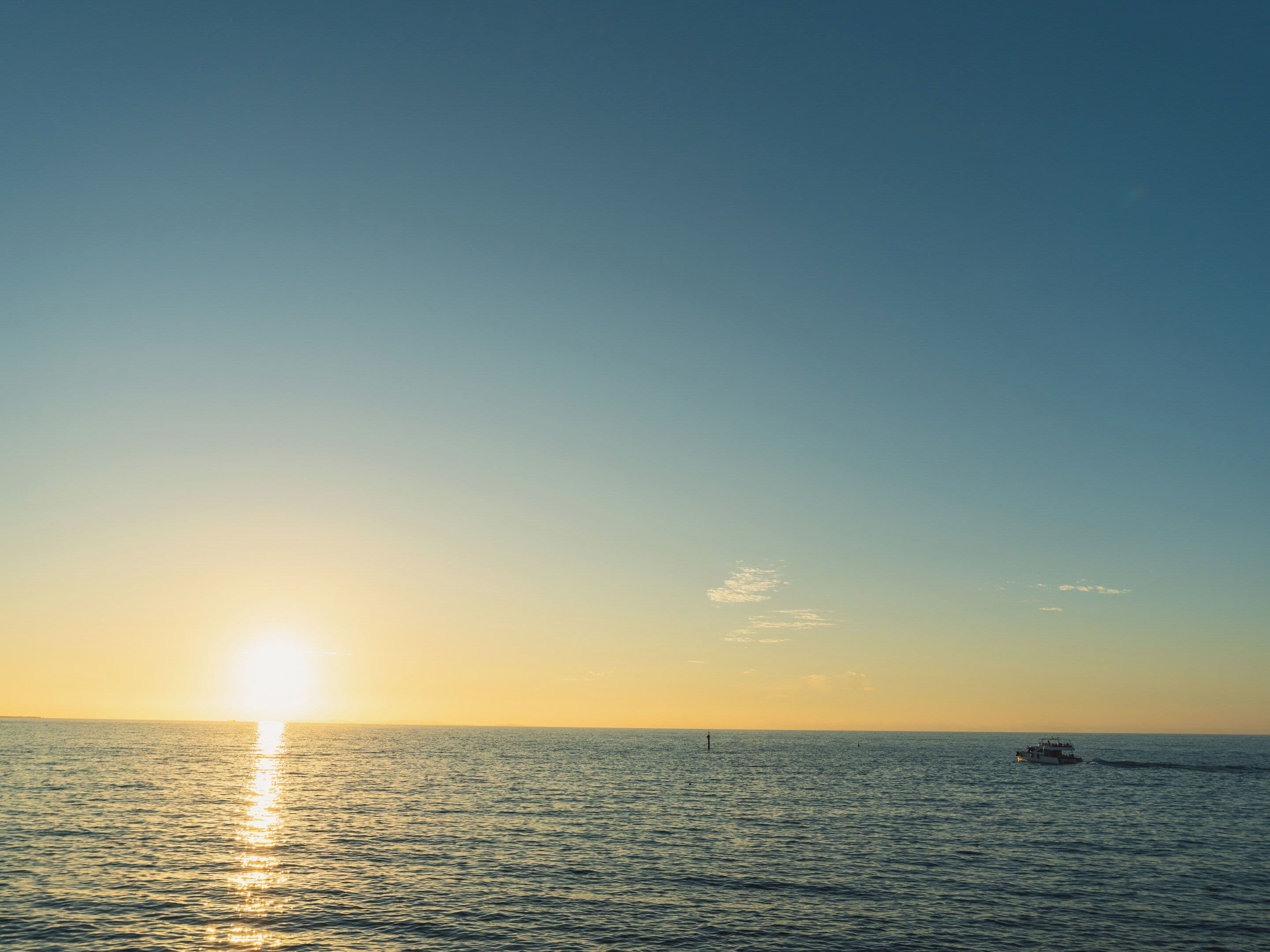 A sunset over a calm sea with a boat in the distance.