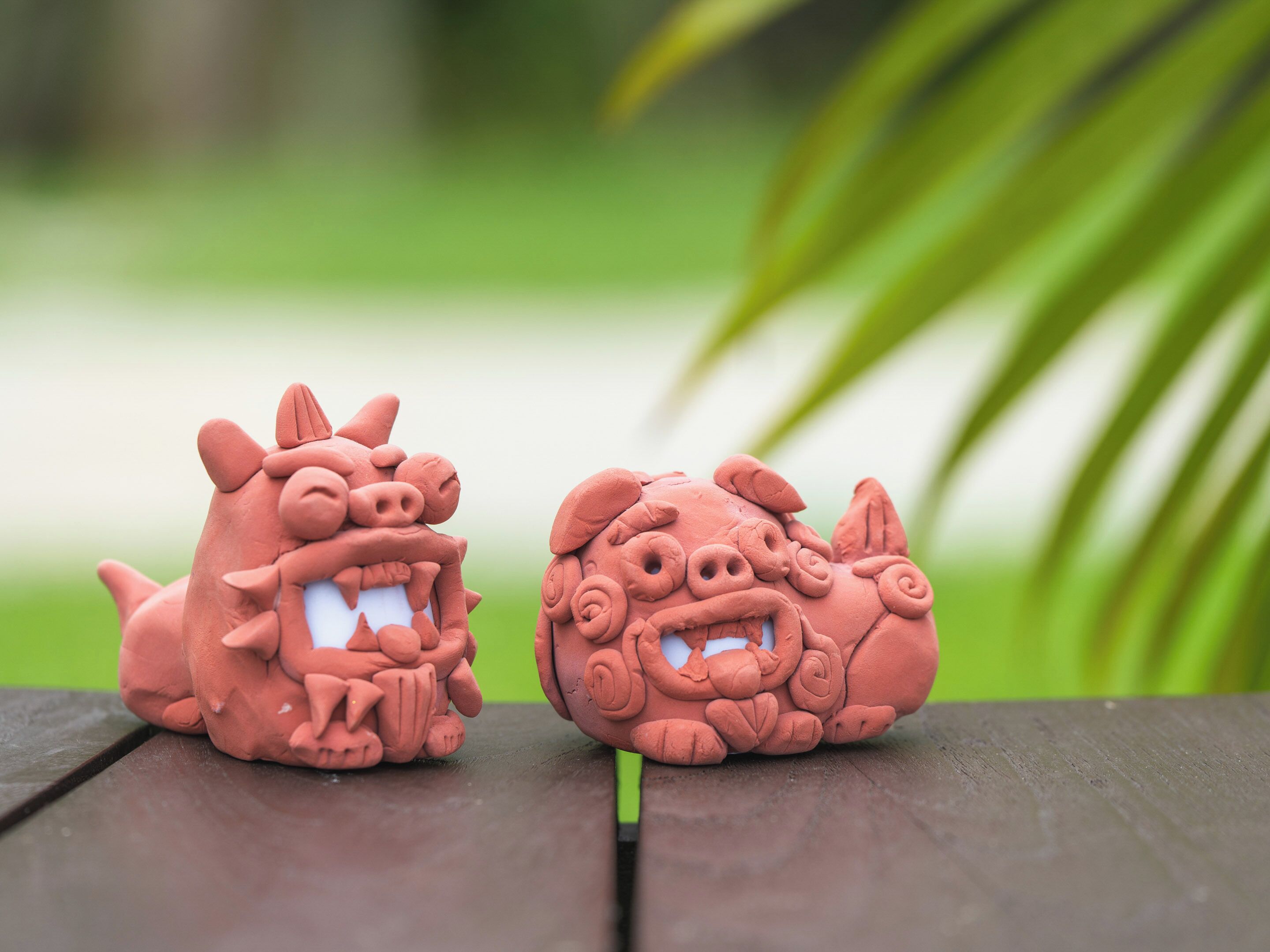 Two terracotta animal figures on a wooden surface with a blurred green background.
