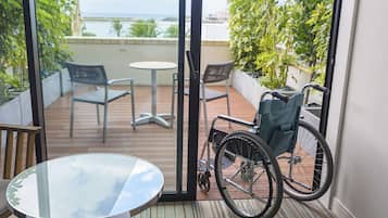 A wheelchair-accessible balcony with a glass table, two chairs, and a view of the sea.