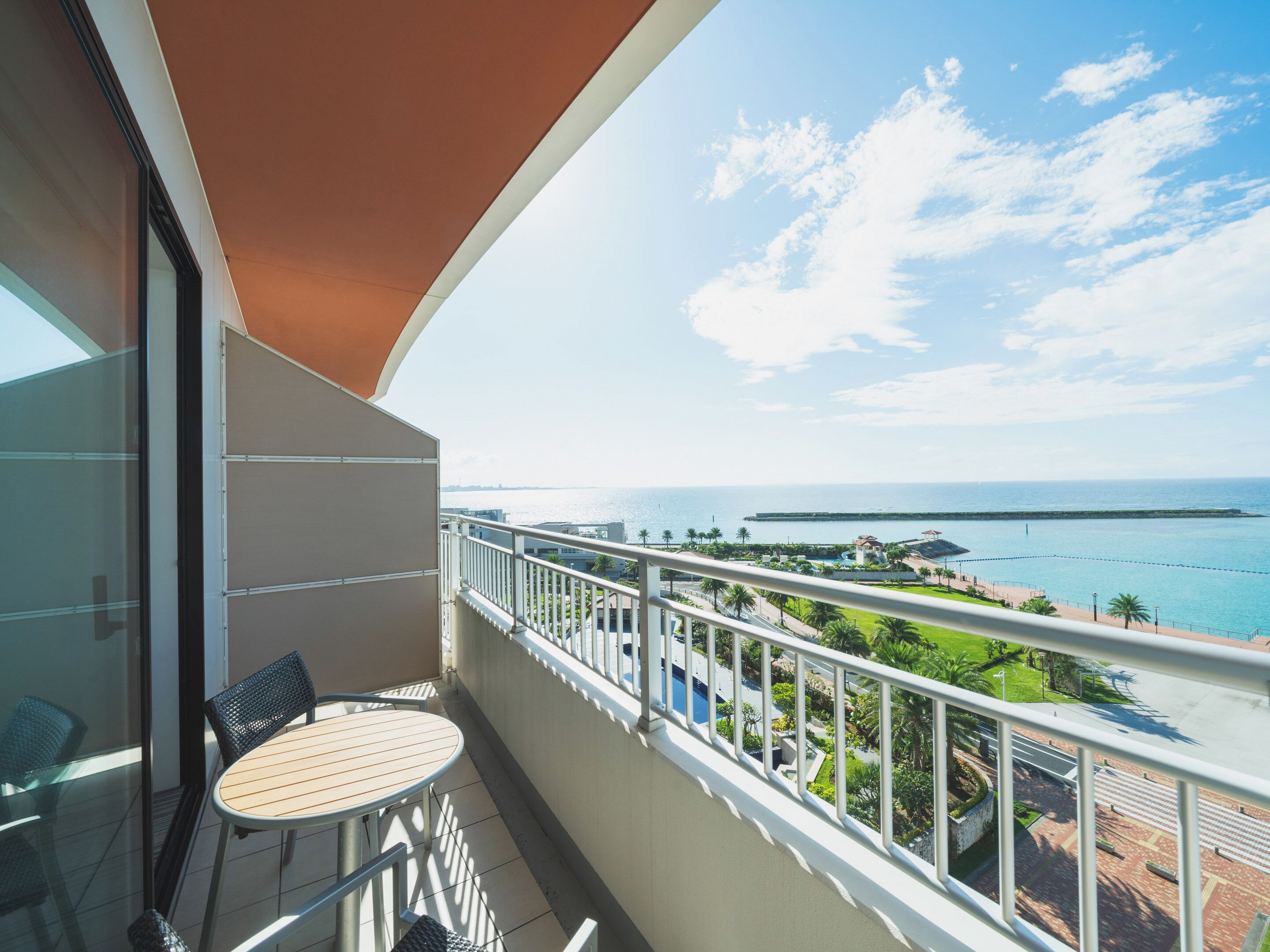 A balcony with a table and chairs, overlooking a coastal view with a clear sky.