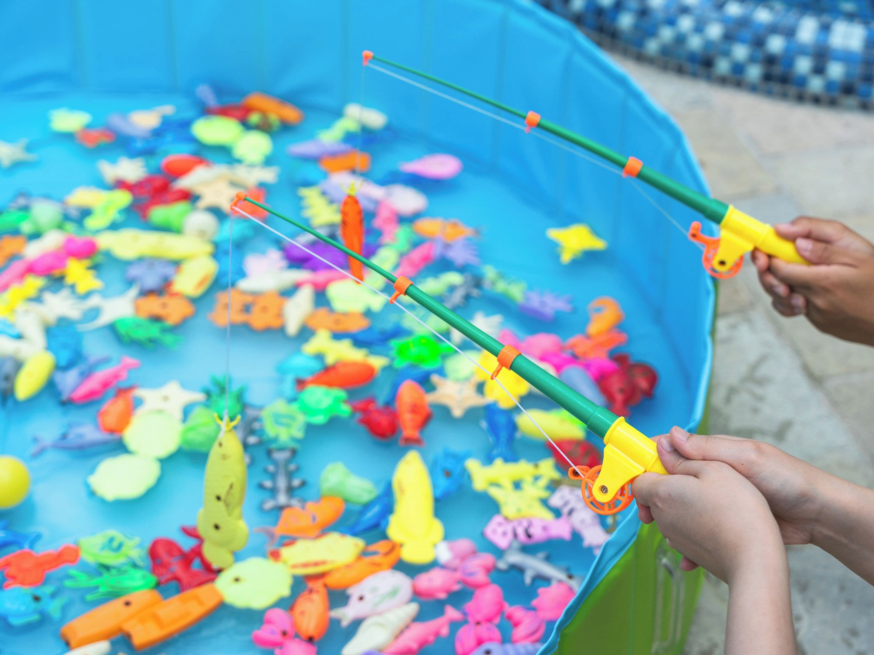 A large blue container filled with colorful plastic fish and a fishing rod.