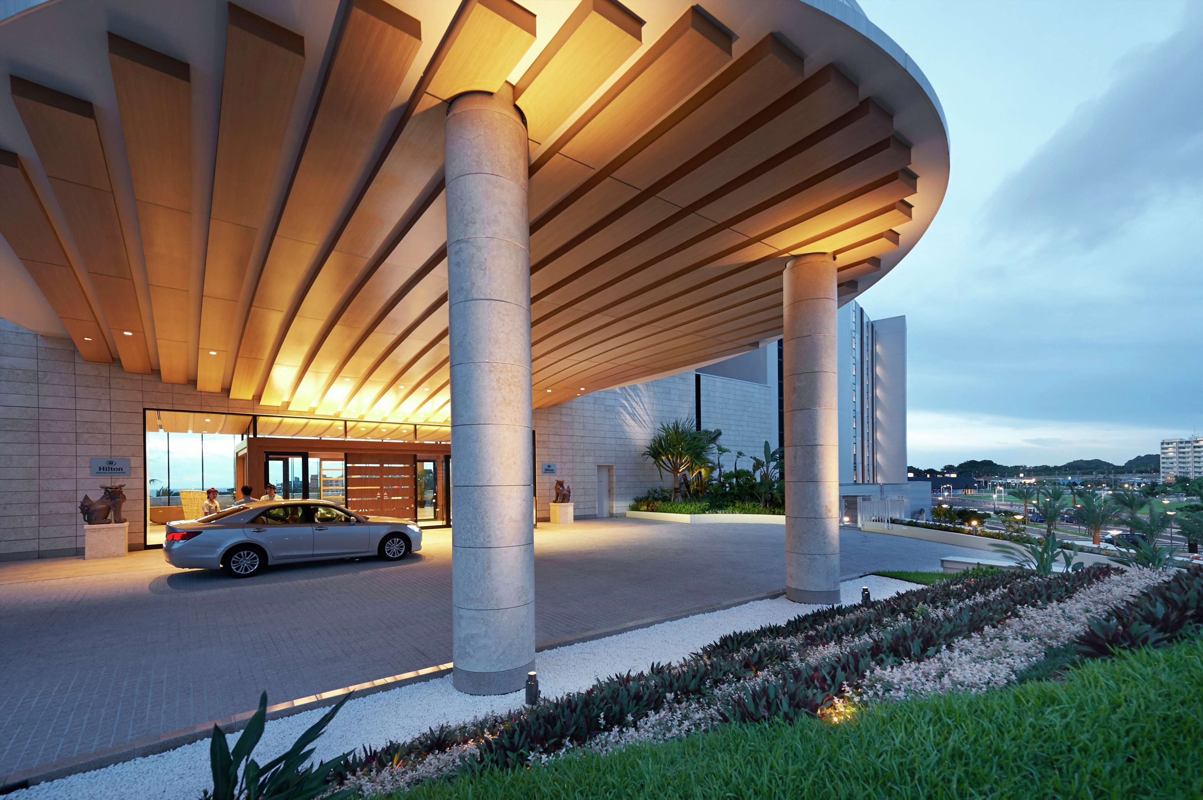 A modern hotel entrance with a curved roof, large columns, and a car parked in front.