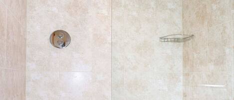Un baño moderno con ducha envuelta en cristal, bañera blanca y paredes con azulejos color beige.