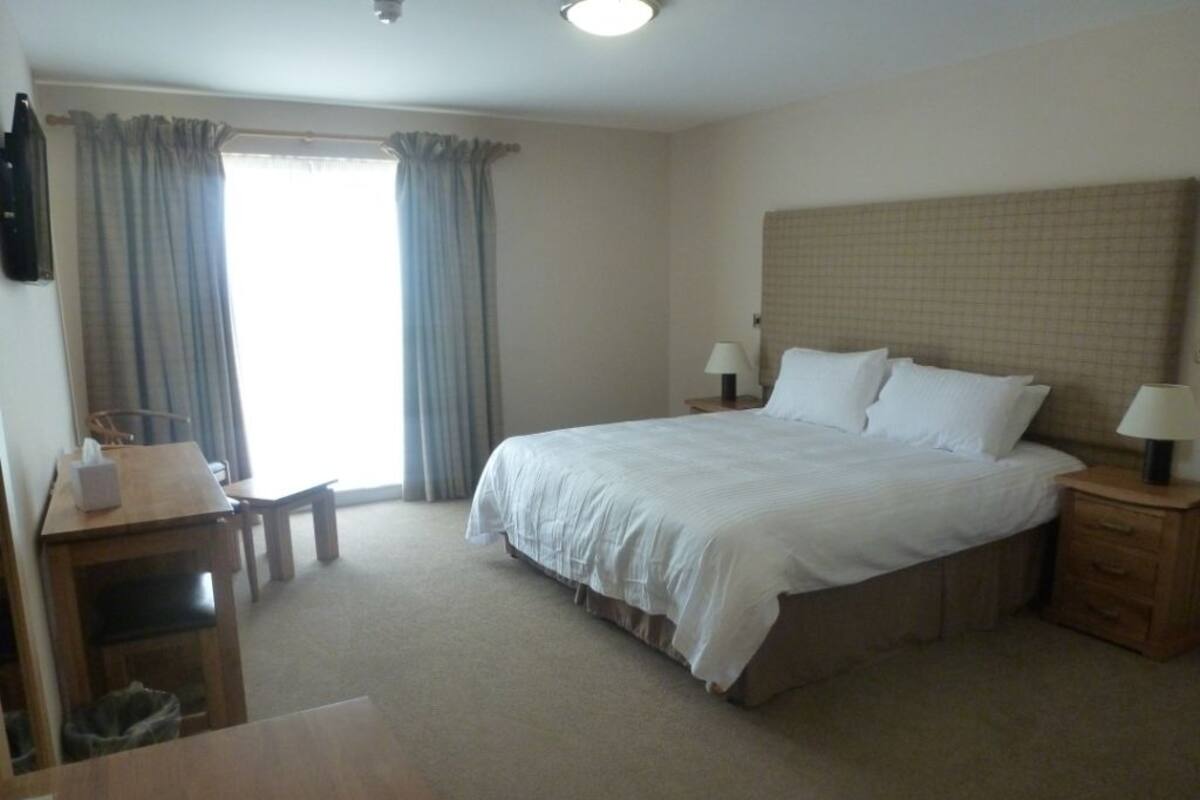 Habitación de hotel con una cama grande, dos mesitas de noche con lámparas, un escritorio de madera y una silla.