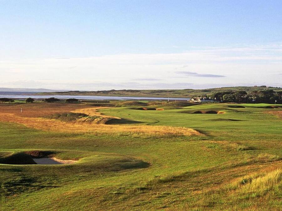 Un campo de golf con búnkeres, una masa de agua y colinas al fondo.