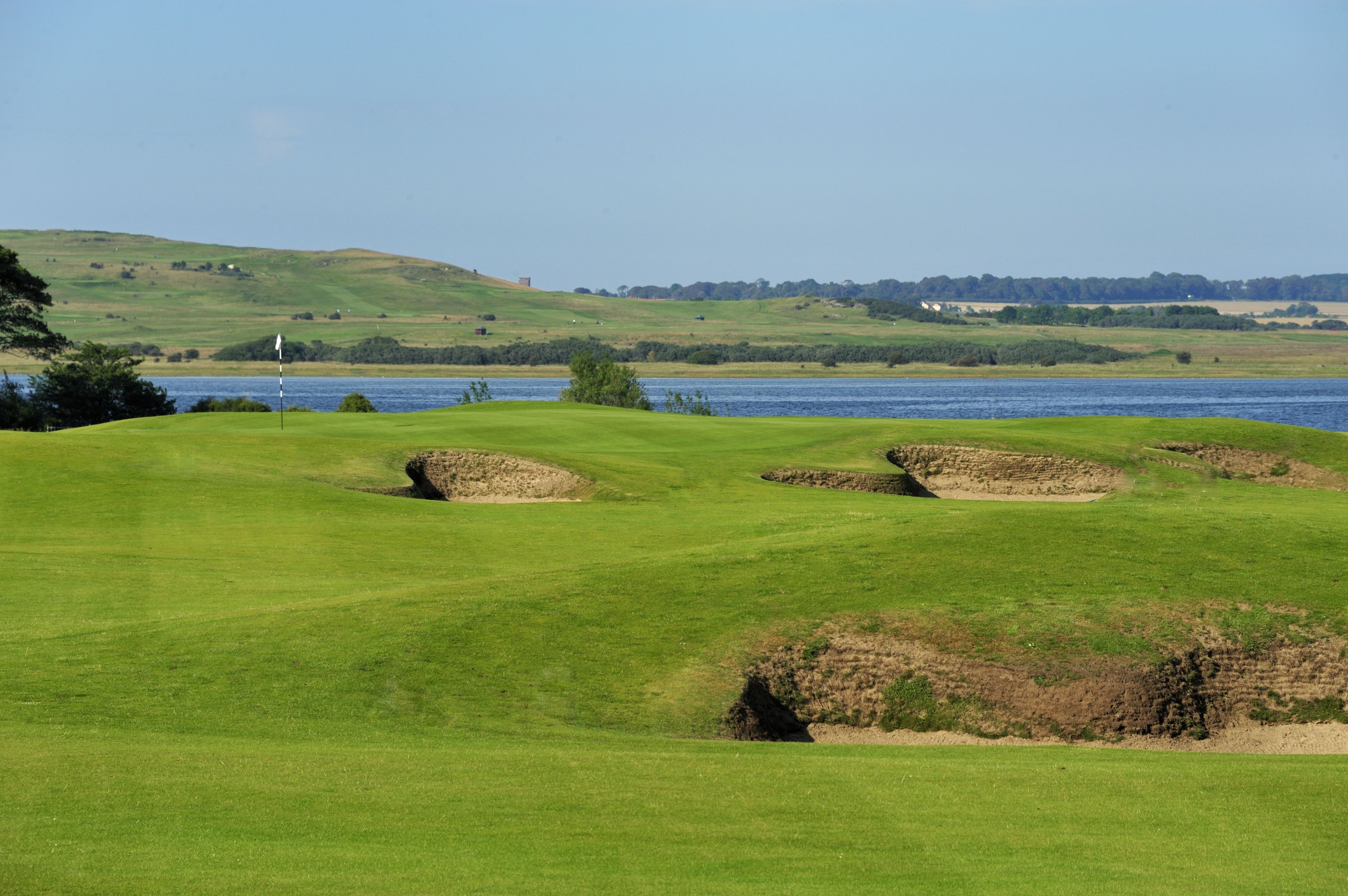 Un parcours de golf avec des bunkers, un drapeau et une étendue d’eau en arri ère-plan.