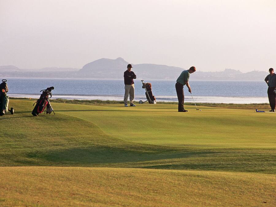 Un campo de golf con vistas al océano y montañas al fondo.