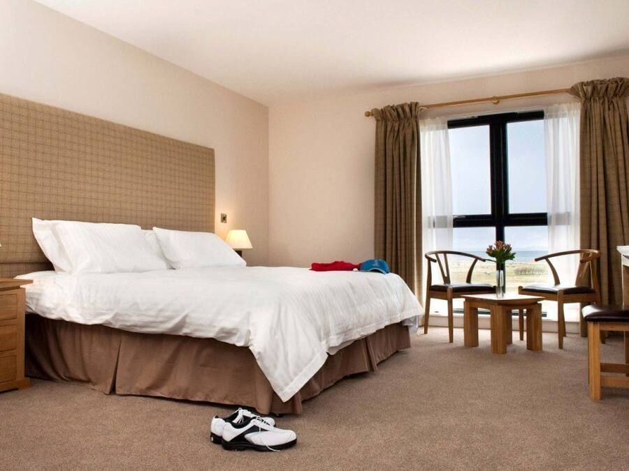 Habitación de hotel con una cama grande, mesitas de noche, un escritorio con sillas y una ventana con cortinas.