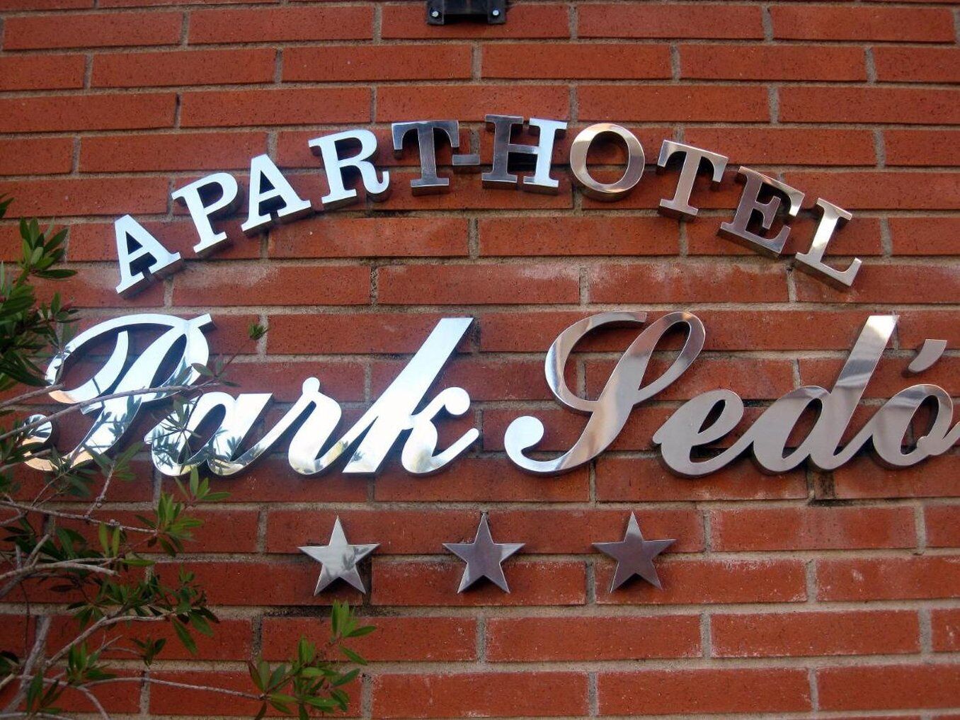Une plaque métallique portant l’inscription « APARTHOTEL Park Sedó » est fixée à un mur de briques.
