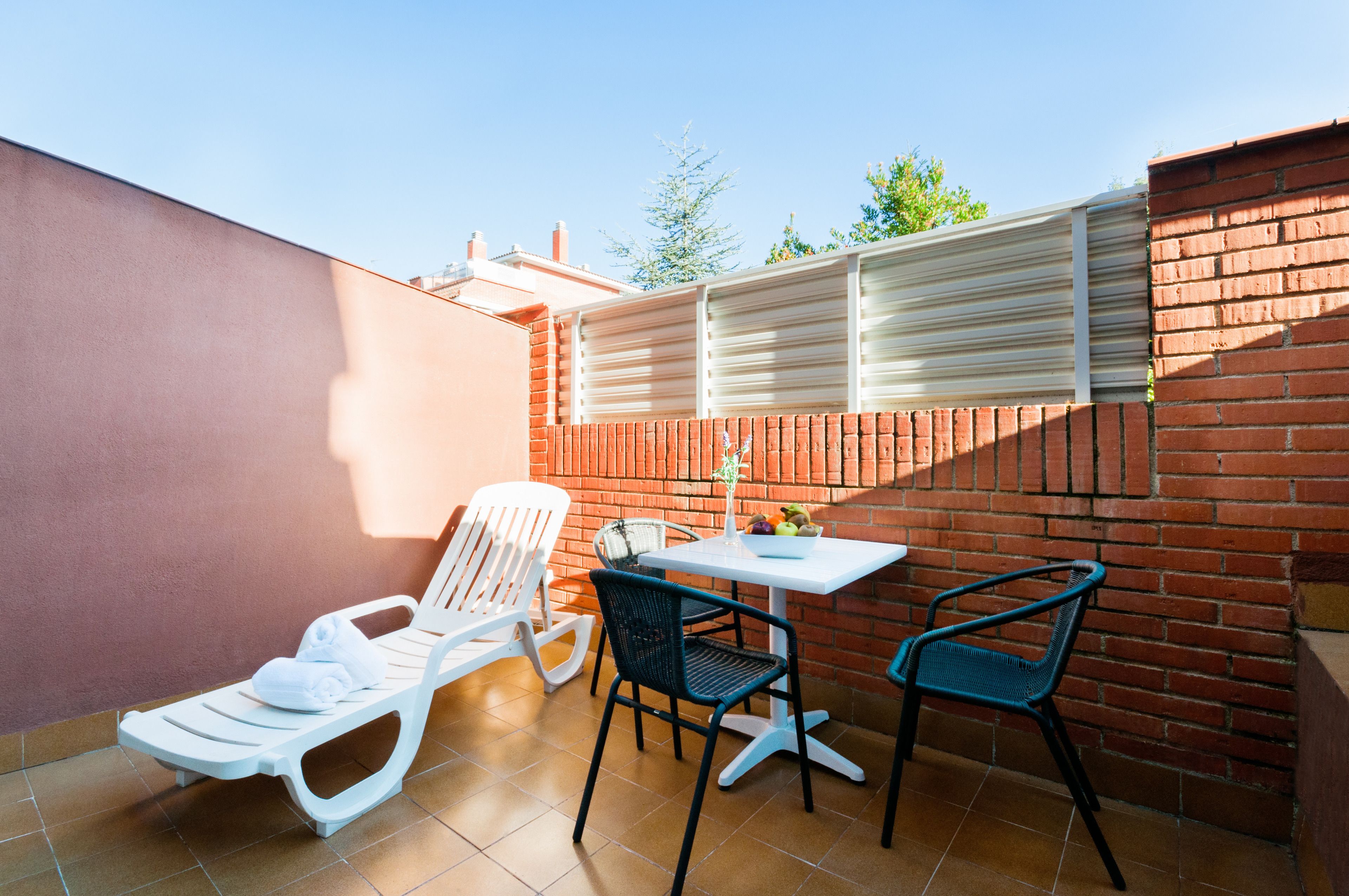 Une terrasse avec une table blanche, deux chaises et un transat.
