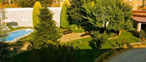 A residential backyard with a swimming pool, a wooden deck, and a variety of trees and shrubs.
