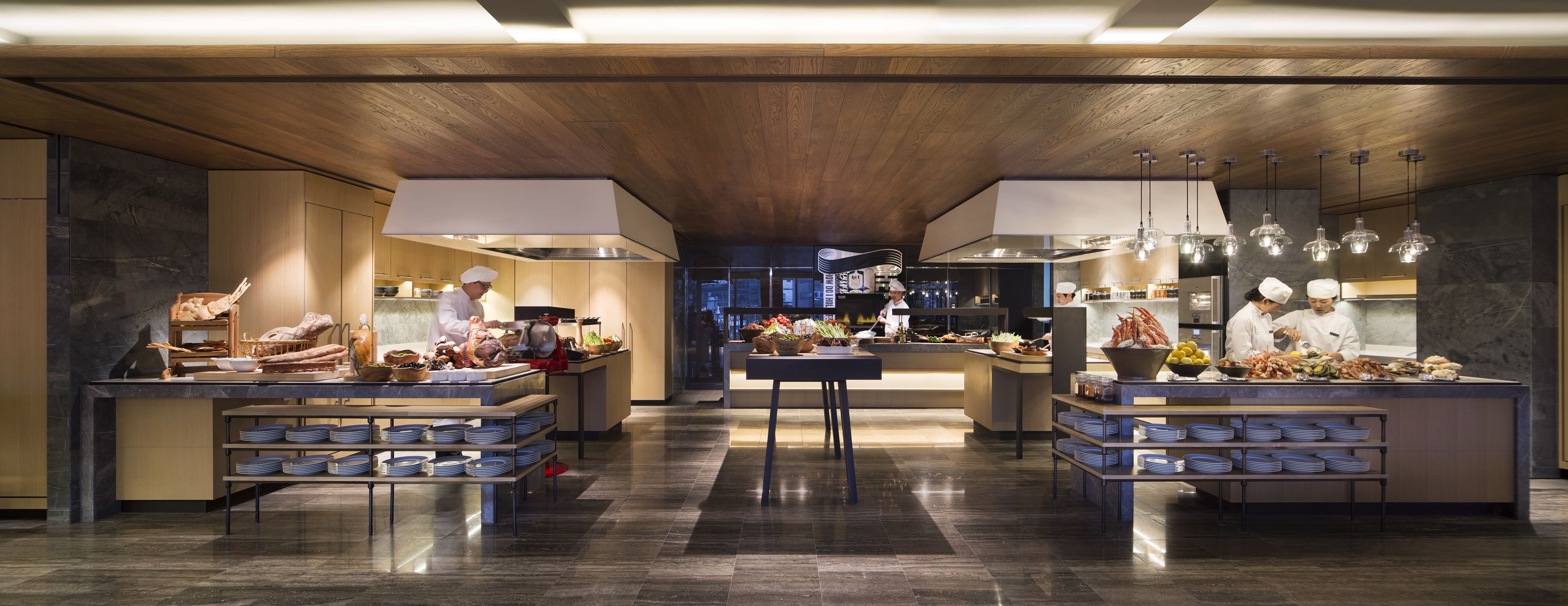 A modern kitchen with chefs preparing food, equipped with stainless steel appliances and wooden accents.