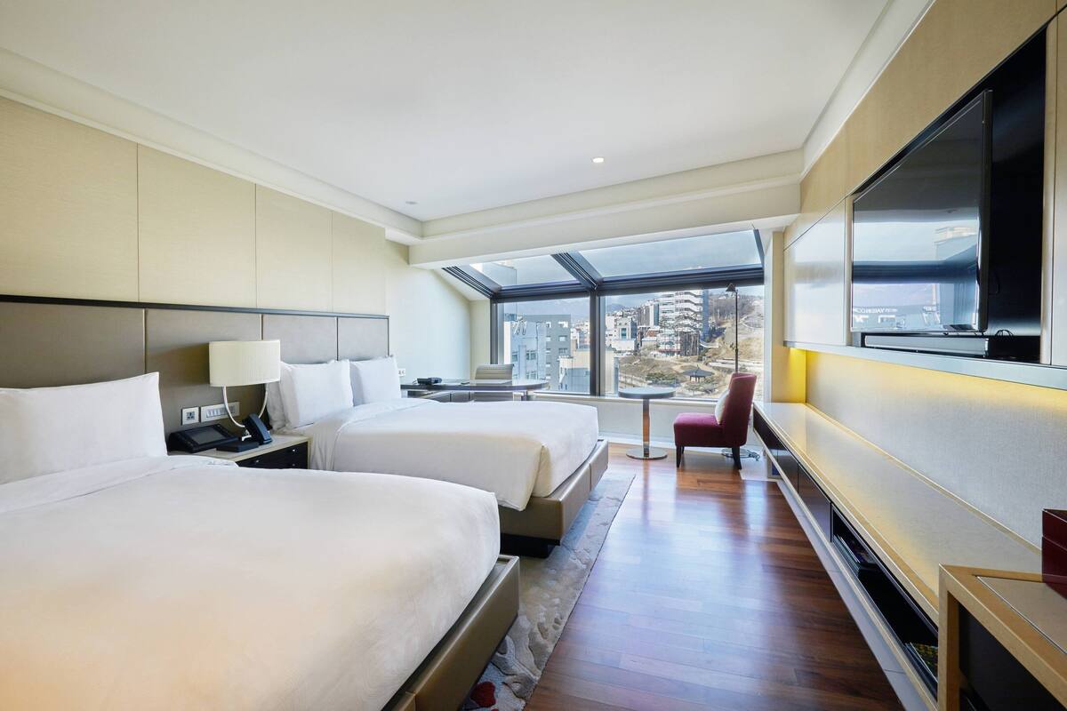 Une chambre d’hôtel avec deux lits, une télévision, un bureau et une fenêtre donnant sur la ville.