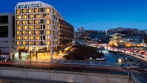 A JW Marriott hotel with a modern design, located near a busy intersection with traffic lights and a traditional building in the background. - JW Marriott Dongdaemun Square Seoul (Seoul)