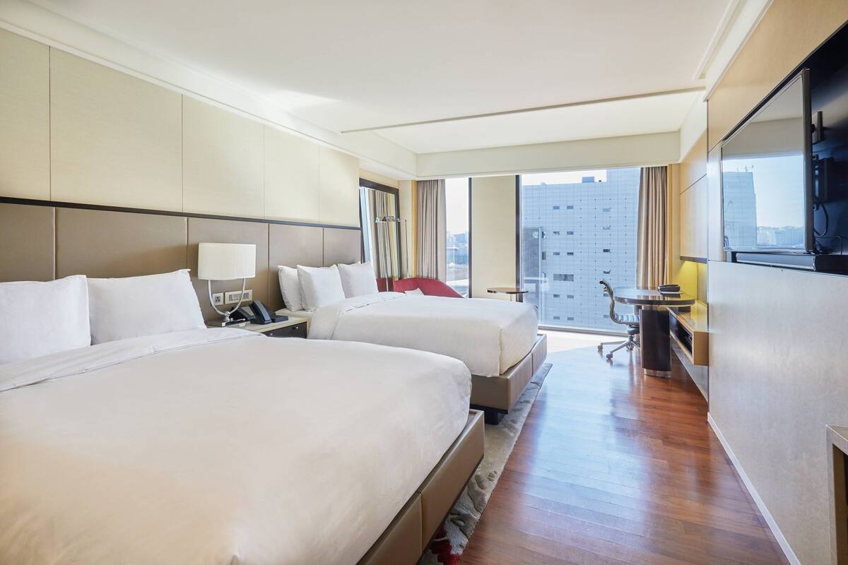 Une chambre d’hôtel avec deux lits, un bureau, une chaise et un téléviseur.
