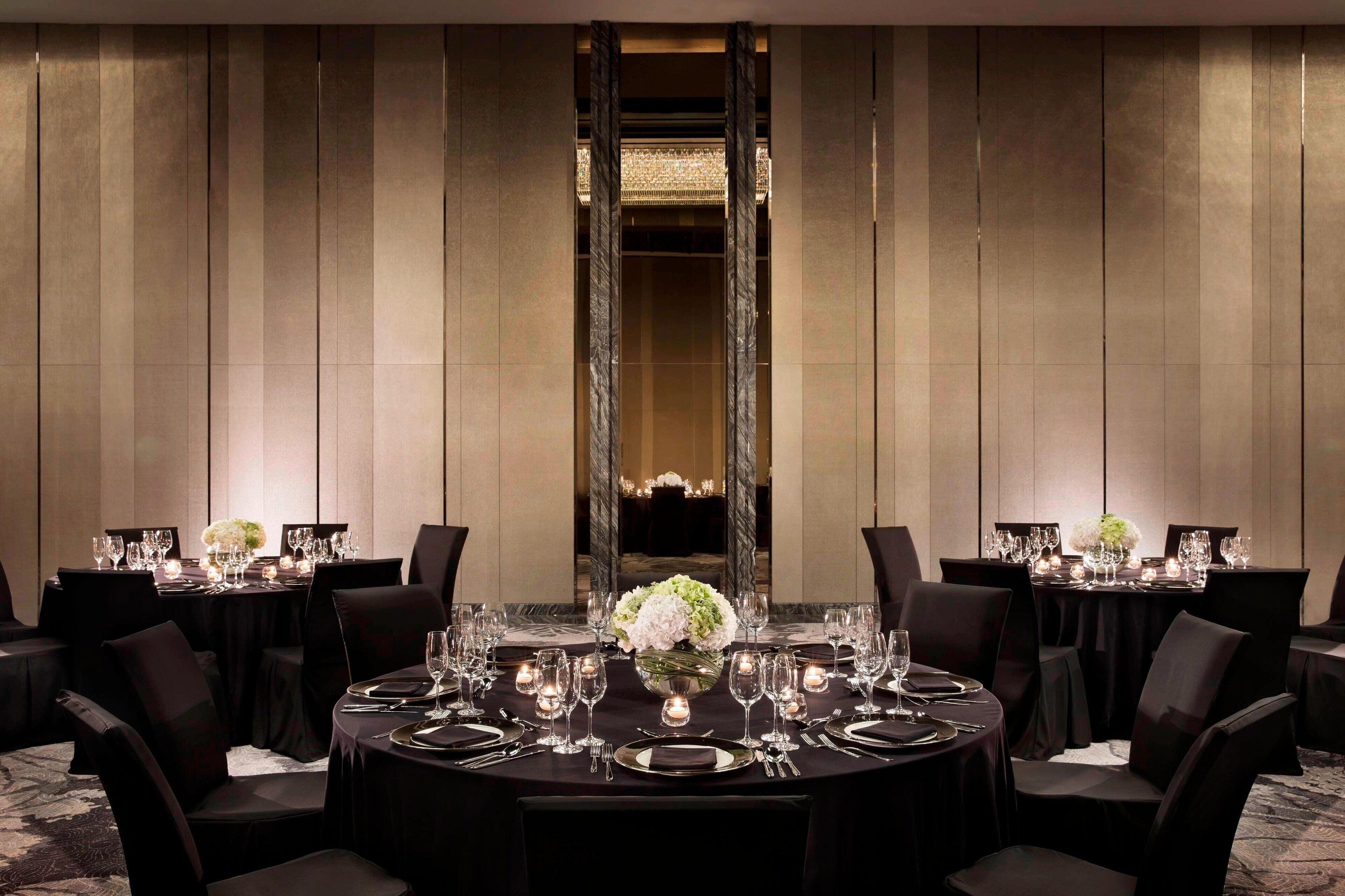 Un comedor elegante con mesas redondas, manteles negros y centros de mesa con flores blancas.