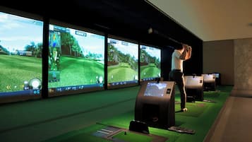 Una sala de simulación de golf con varias pantallas mostrando un partido de golf, una persona practicando swings y un suelo cubierto de alfombra verde.