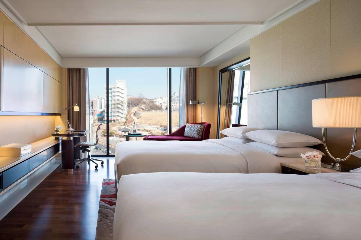 Une chambre d’hôtel avec deux lits, un bureau, une chaise et une vue sur la ville.