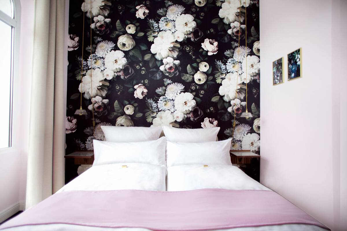 A bedroom with a floral wallpaper, a bed with white linens, and two bedside tables.