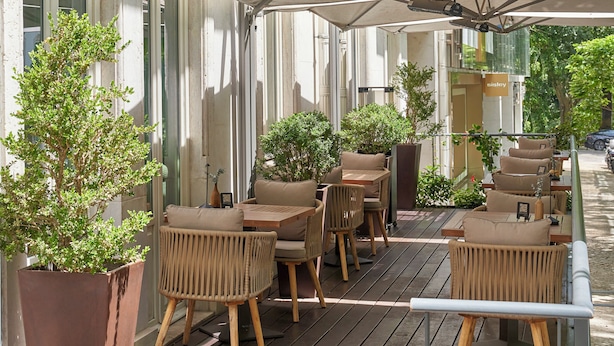 Un espacio exterior con asientos de mimbre, una gran sombrilla, plantas en macetas y una terraza de madera.