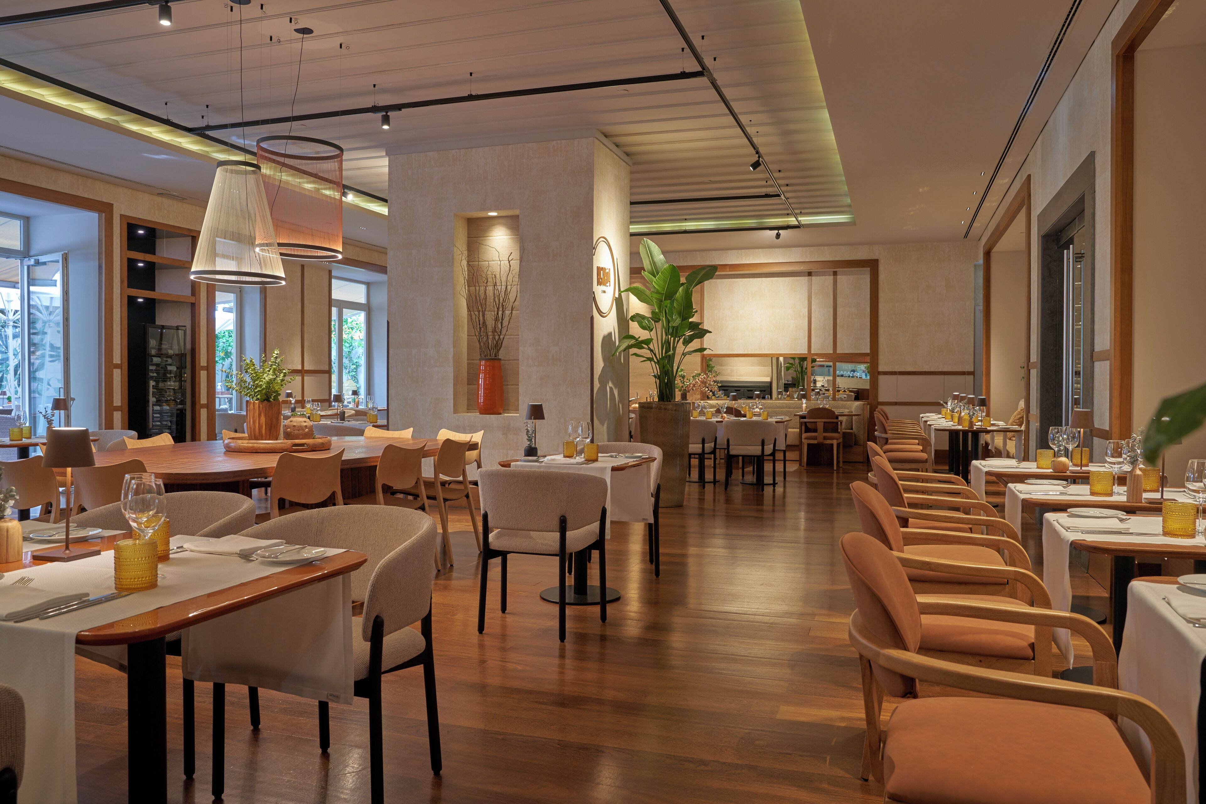 A spacious restaurant with multiple dining areas, wooden flooring, and modern lighting fixtures.