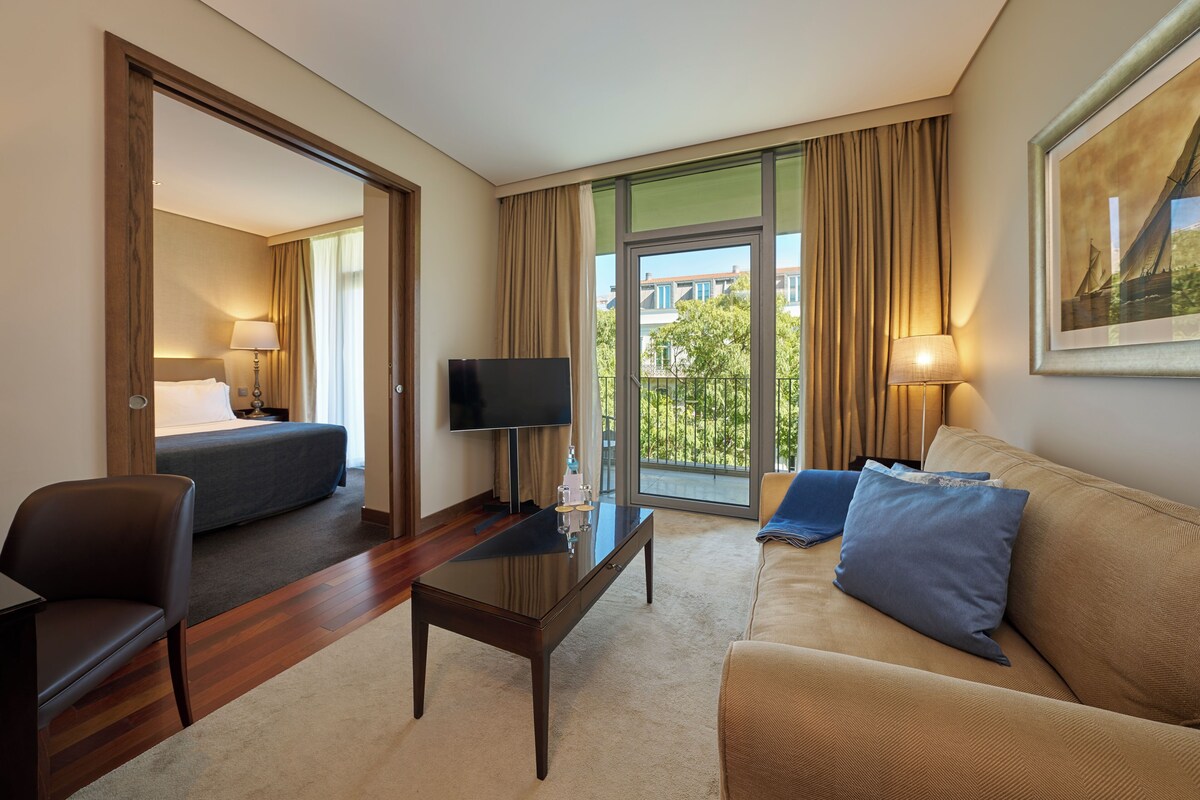 A hotel room with a bed, a TV, a sofa, a coffee table, and a balcony with a view.