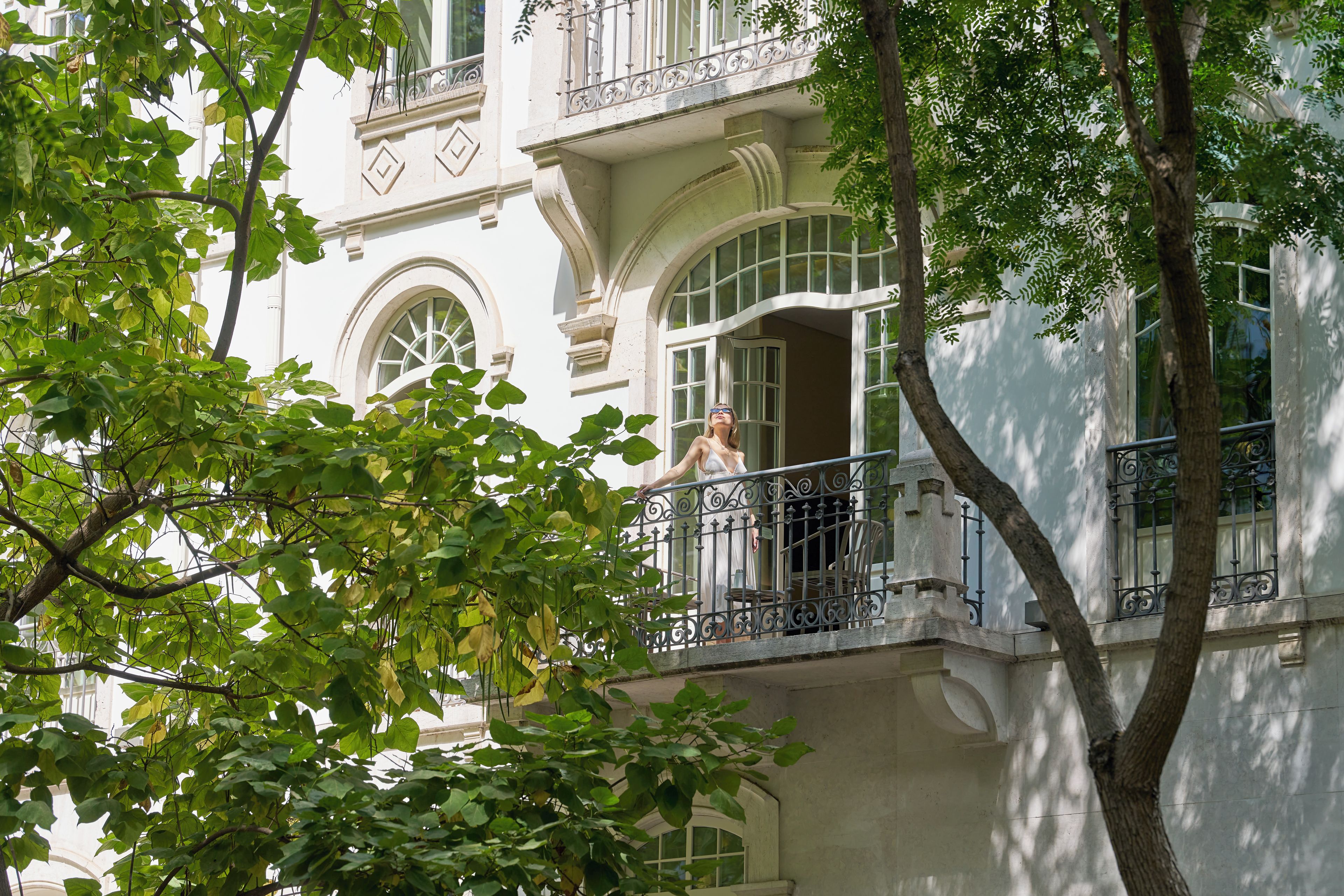 Ένα κτίριο με μπαλκόνι, μεγάλα παράθυρα και ένα δέντρο στο προσκήνιο.